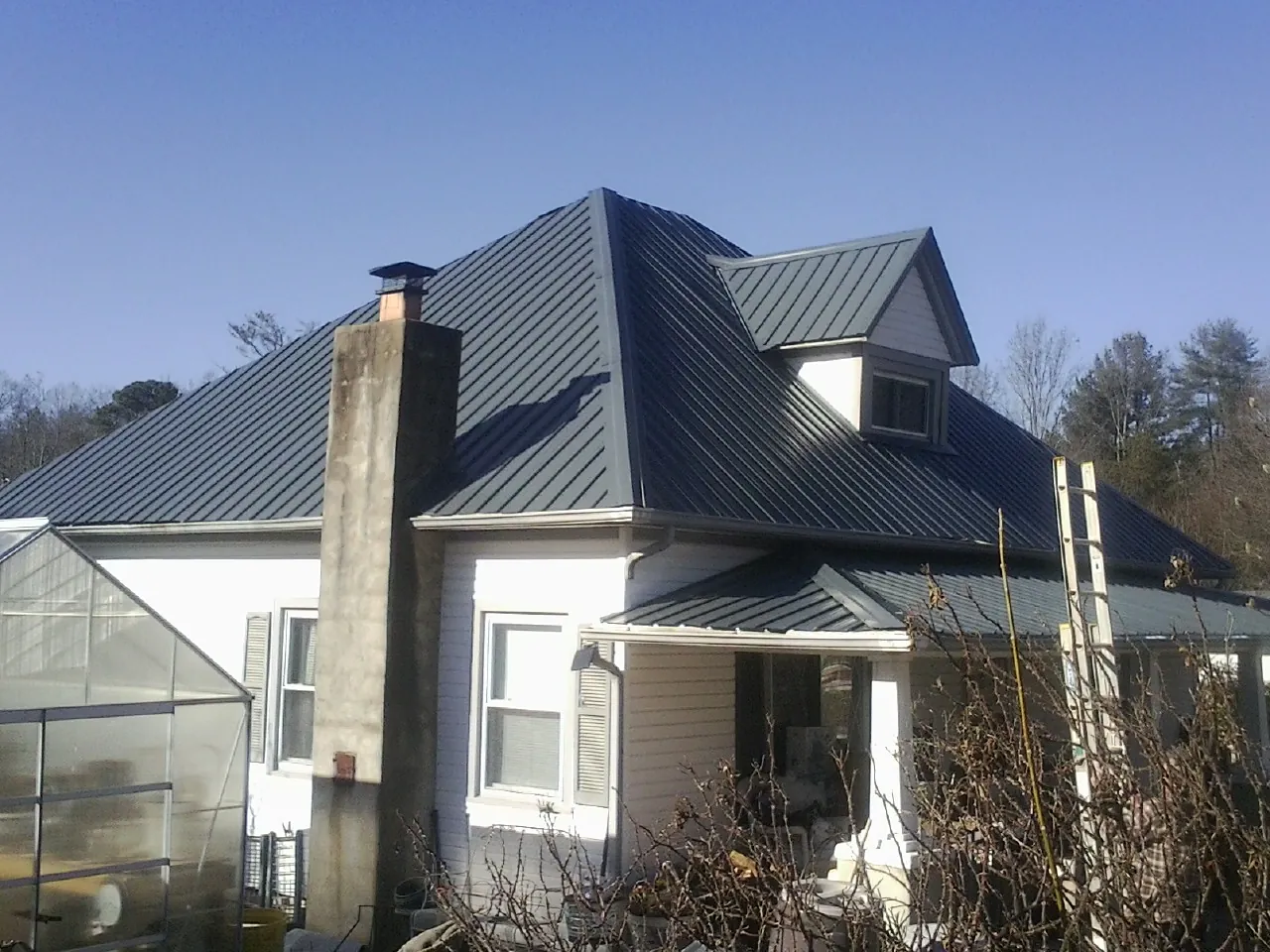 Dark blue standing seam metal roof on a white farmhouse with dormer — Slate & Tile Roof Repair by Roofing Brothers in Orwell