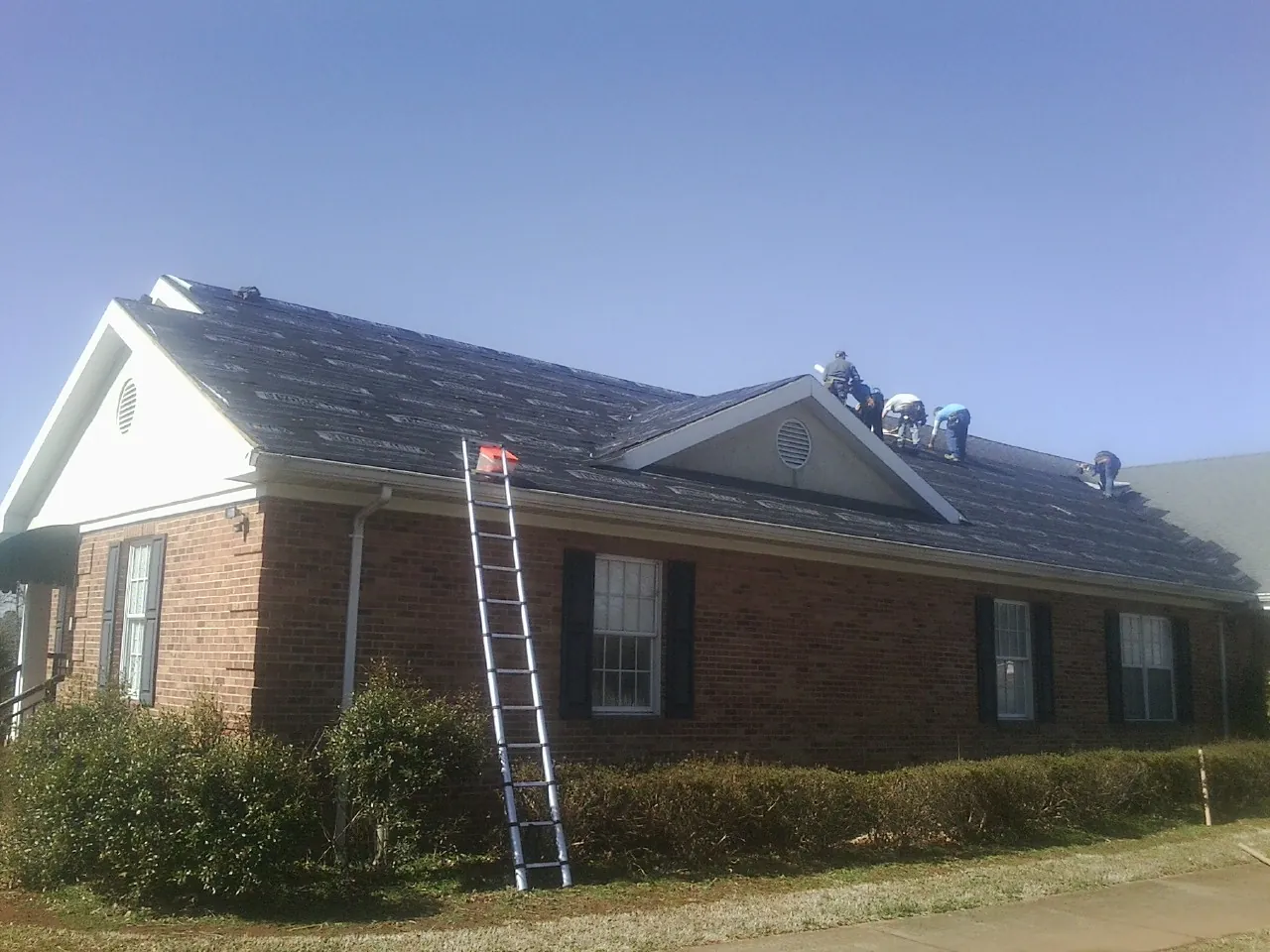 Crew tearing shingles off a brick ranch roof with a ladder set — Emergency Roof Repair work by our crew in Orwell