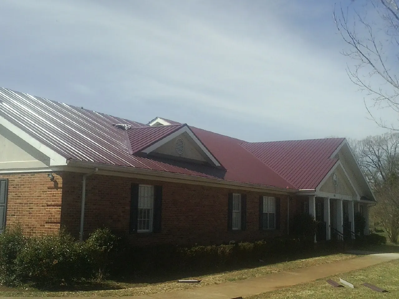 Red metal roof with gabled entries on a long brick building, from a Hail Damage Roof Repair job in Orwell