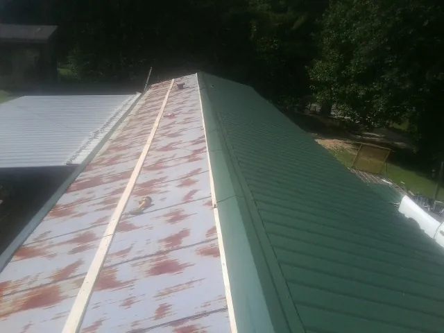 Old rusted panels beside newly installed green metal roofing — Wind Damage Roof Repair by Roofing Brothers in Orwell