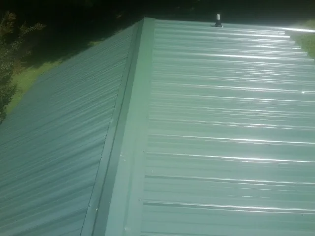 New green metal panels meeting at the ridge of a roof — Flat Roof Repair work by our crew in Orwell