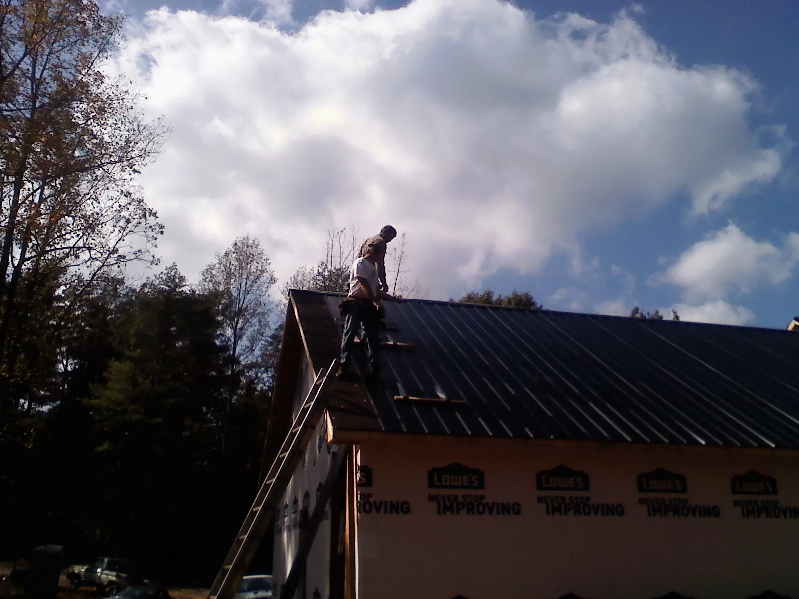 Roofer fastening dark metal panels high against a cloudy sky, from a Roof Inspection job in Orwell