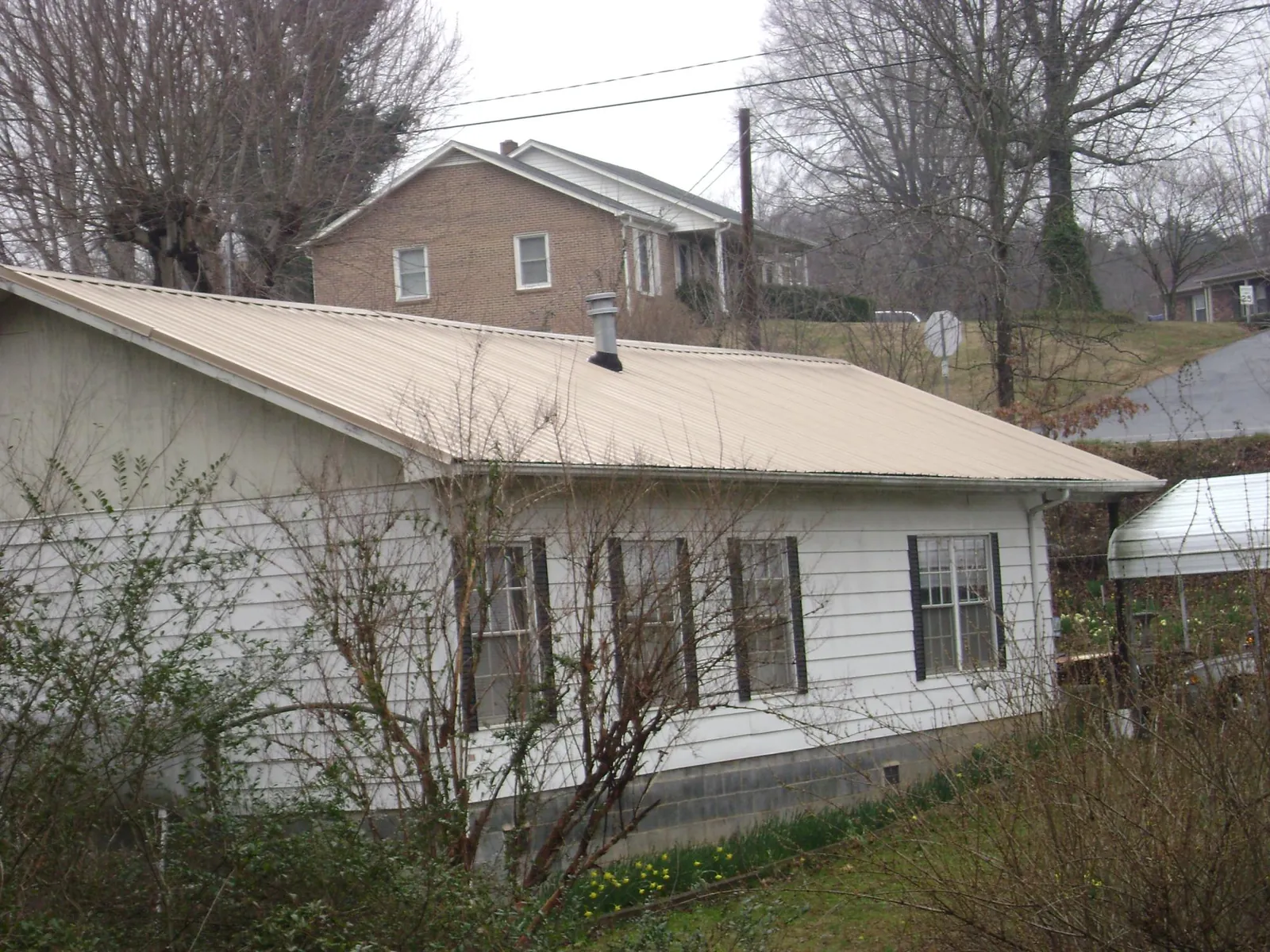 Tan metal roof on a white sided house set into a hillside — Commercial Roofing by Roofing Brothers in Orwell