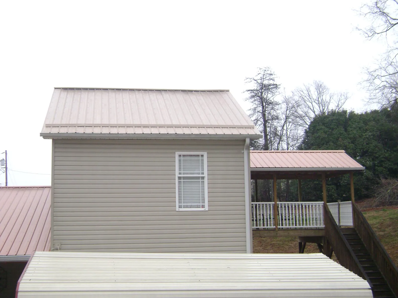 Tan metal roofs on a two story addition and attached porch, from a Roof Replacement job in Orwell